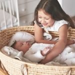 Sister and brother. Girl with baby boy in wicker cradle. Happy childhood. Children room