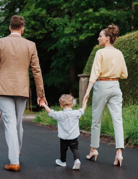 Young family with little son on walk in city park after work.